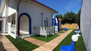 Um edifício branco com arcos azuis, um deck de madeira e um pequeno jardim com um escorrega.