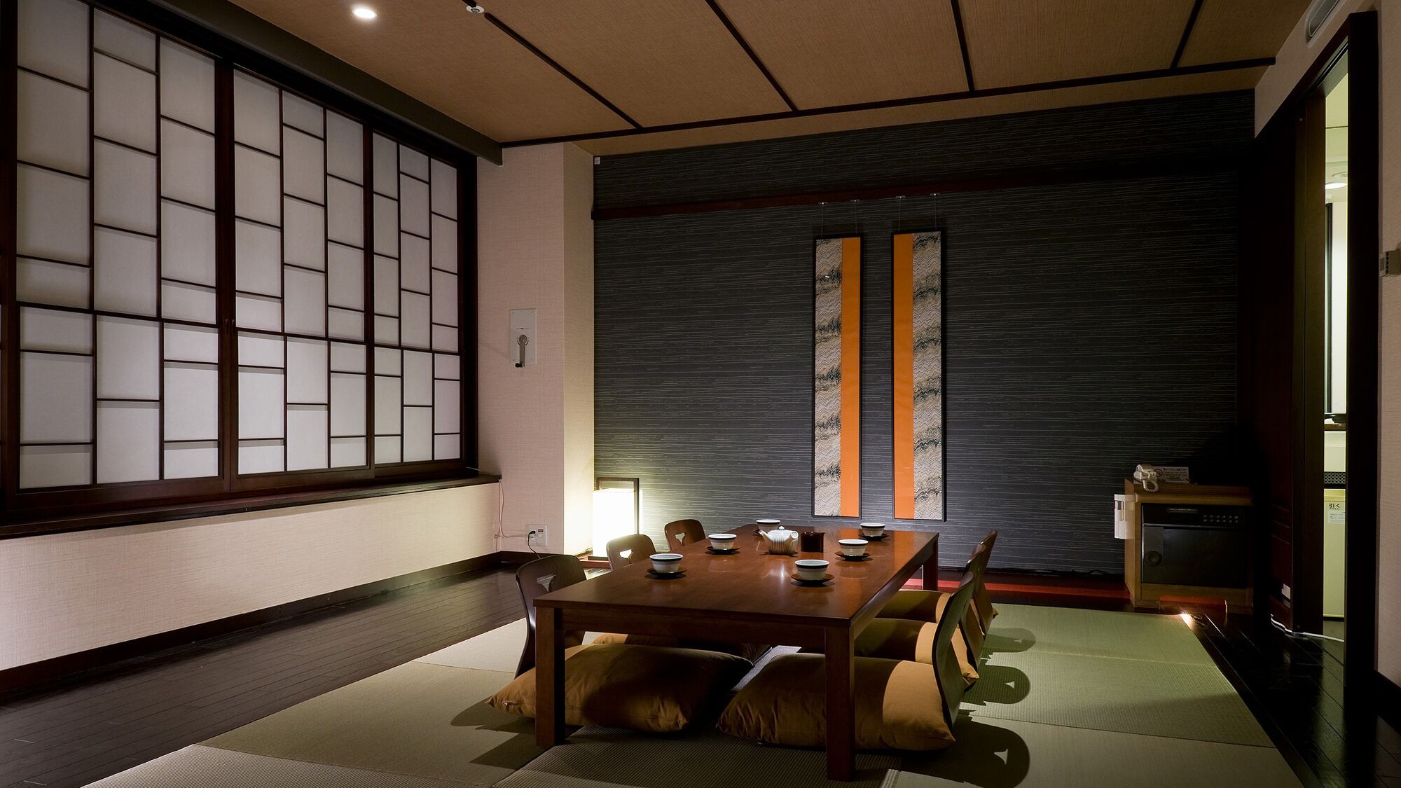 A traditional Japanese-style room with tatami flooring, a low table with tea set, sliding doors, and a dark textured wall.