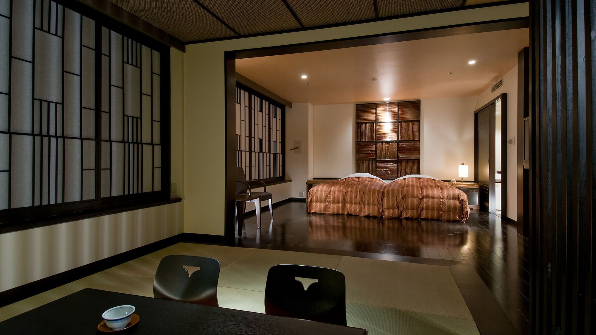 A traditional Japanese-style room with tatami flooring, a low table with a bowl, and a bed with a striped bedspread.