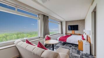 A hotel room with a bed, a sofa, a small table, a TV, and a window with a view of greenery.