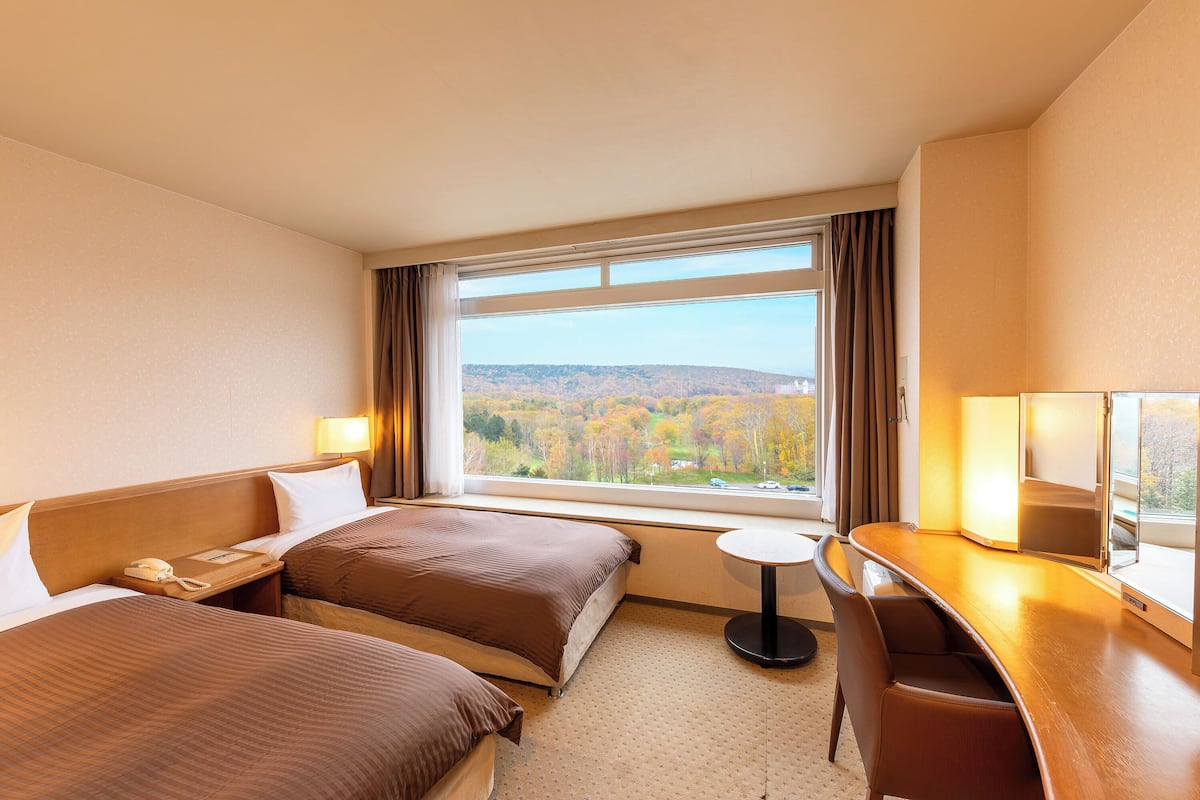 Une chambre d’hôtel avec deux lits, un bureau et une vue sur le feuillage automnal.