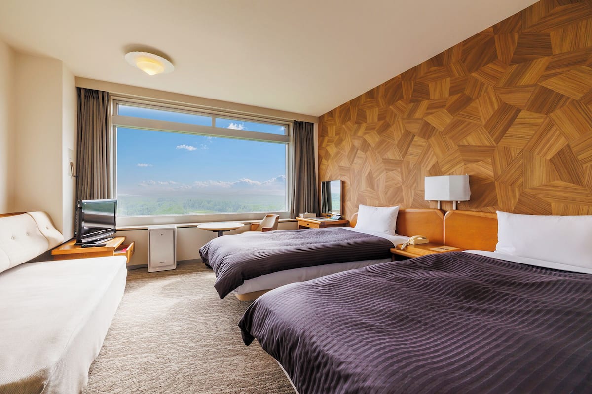 Une chambre d’hôtel avec deux lits, une télévision, un bureau et une grande fenêtre donnant sur un beau paysage.