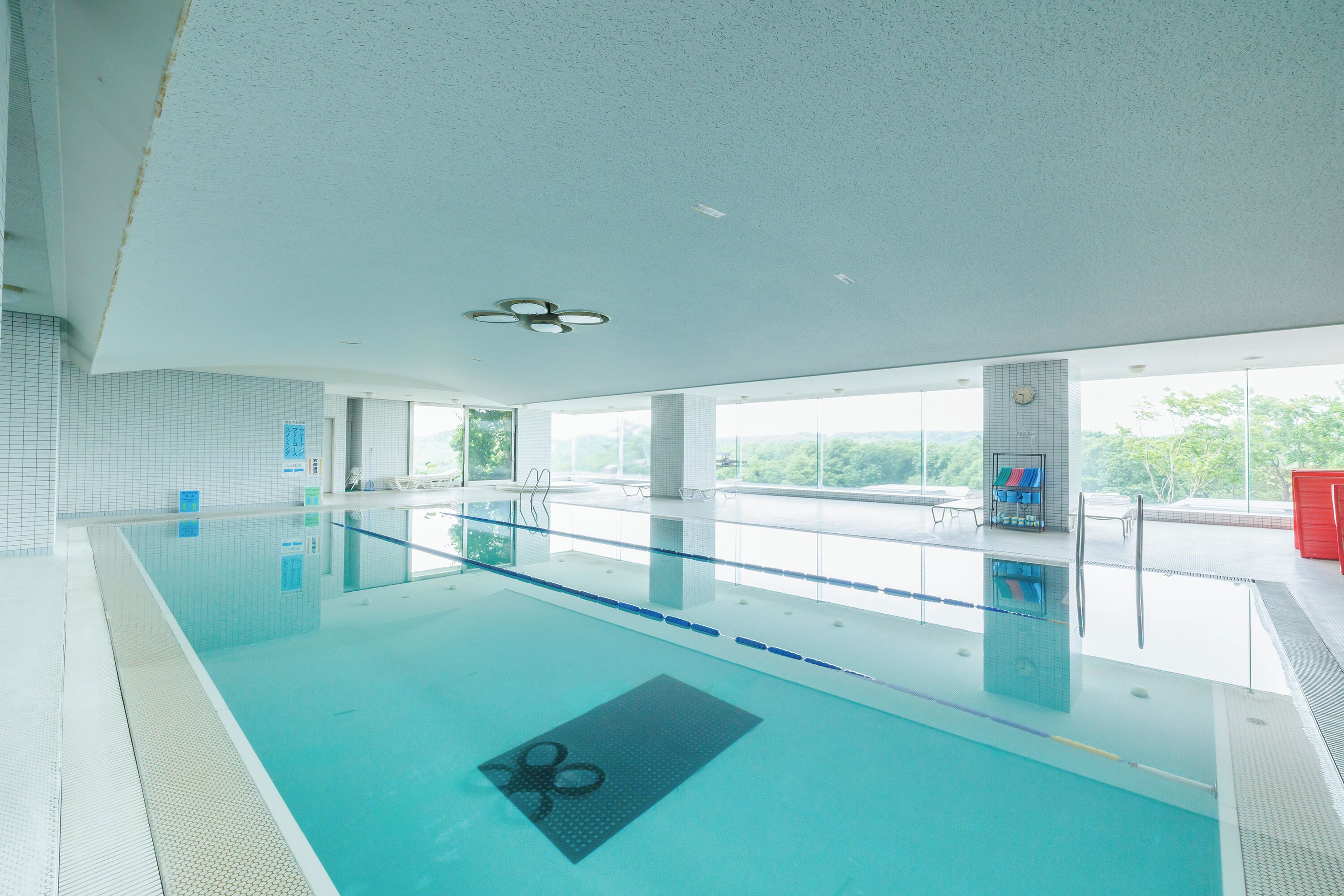 Ein Innenpool mit klarem Wasser, einem Deckenventilator und großen Fenstern mit Blick ins Freie.
