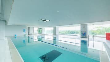 Ein Innenpool mit klarem Wasser, einem Deckenventilator und großen Fenstern mit Blick ins Freie.