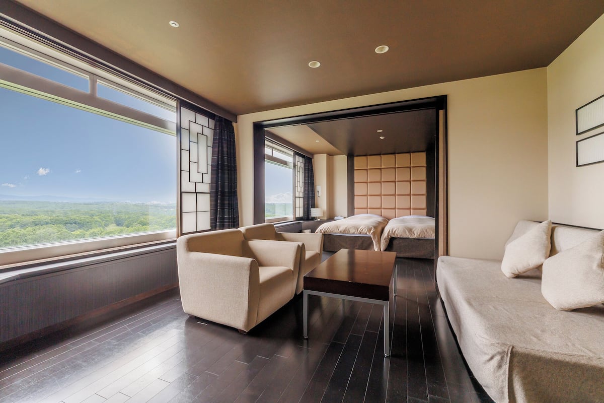 Un salon moderne avec un canapé, des fauteuils et une table basse. Une grande fenêtre offre une vue sur l’extérieur.