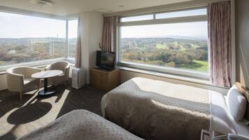 A hotel room with two beds, a TV, a desk with a chair, and a view of a landscape.