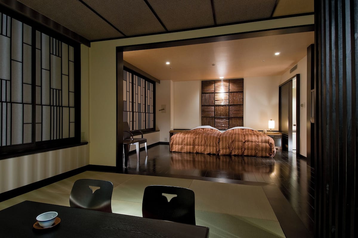 Une pièce de style japonais traditionnel, avec un sol recouvert de tatamis, une petite table et un bol, ainsi qu'un lit recouvert d'une couverture à rayures.