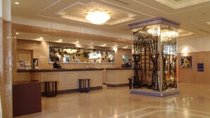 A hotel lobby with a reception desk, a decorative column, and a tiled floor.