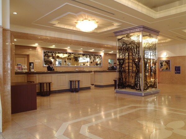 A hotel lobby with a reception desk, a decorative column, and a tiled floor.