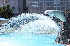 Una statua di un delfino salta fuori da una piscina, con schizzi d'acqua tutt'intorno.