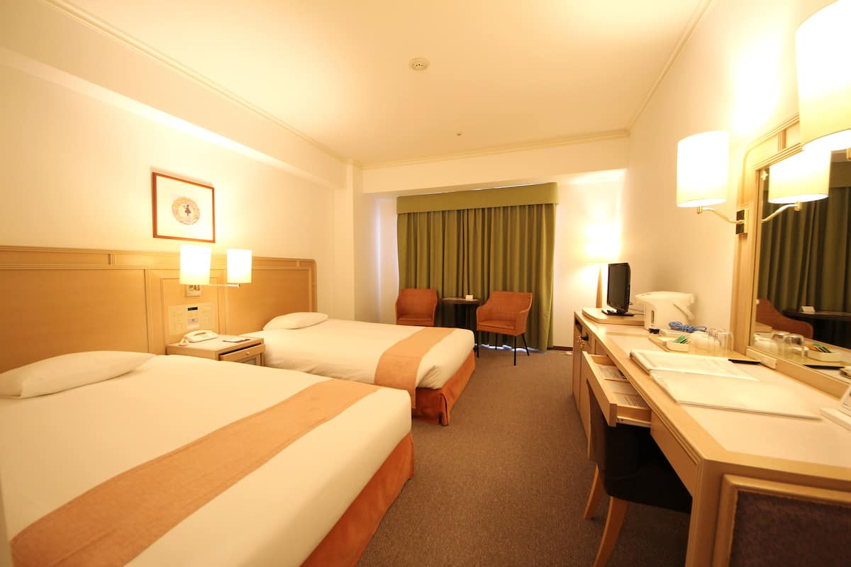 Una habitación de hotel con dos camas, un escritorio con silla, un teléfono y un espejo.