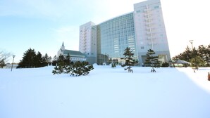 A modern hotel with a glass facade, surrounded by snow-covered ground and trees.