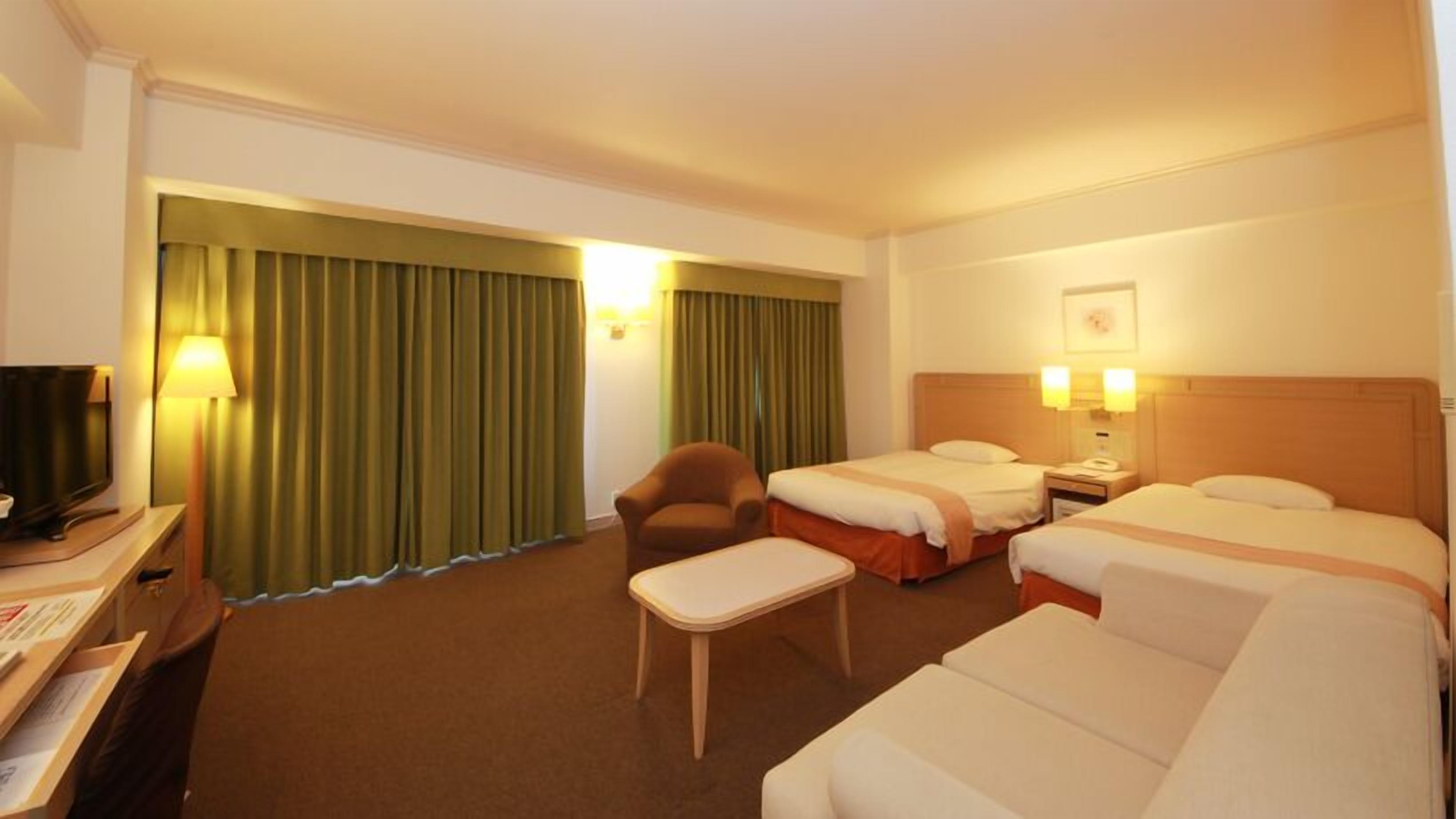 A hotel room with two beds, a desk with a television, a chair, and a small table.