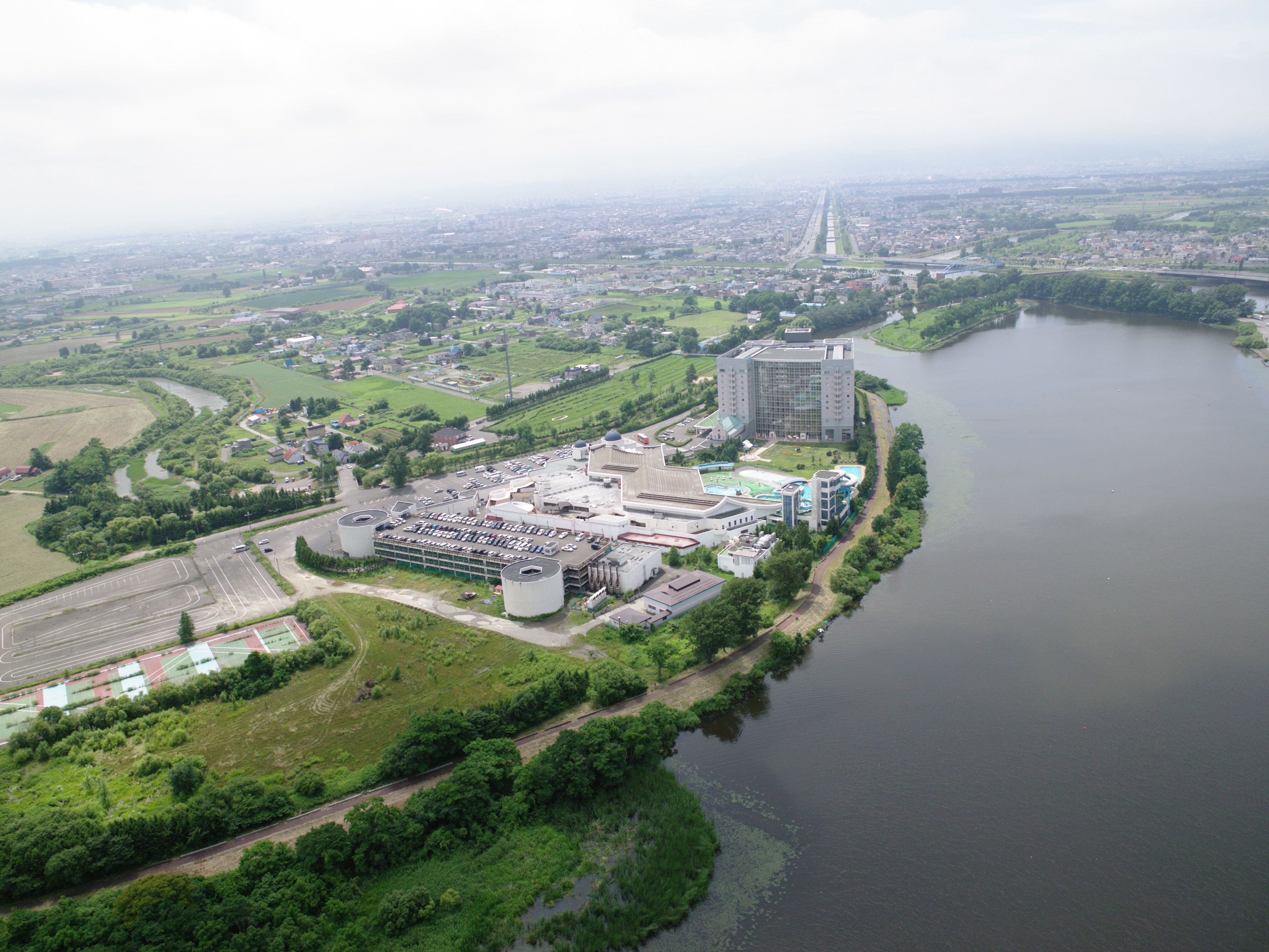 An industrial area with a large parking lot, a river, and a bridge in the background.