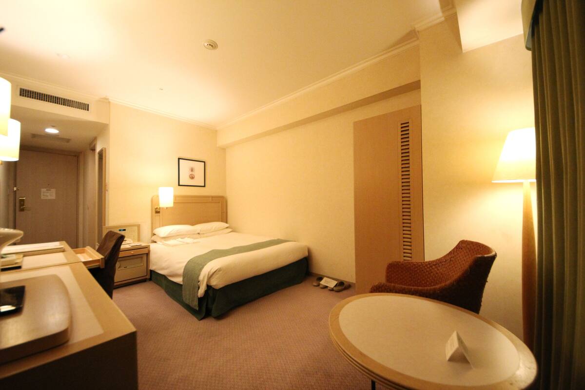 Habitación de hotel con cama, mesita de noche, silla y una pequeña mesa redonda.