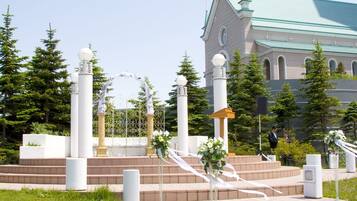 A church with a green roof and white columns, surrounded by a paved area with steps and a small garden.
