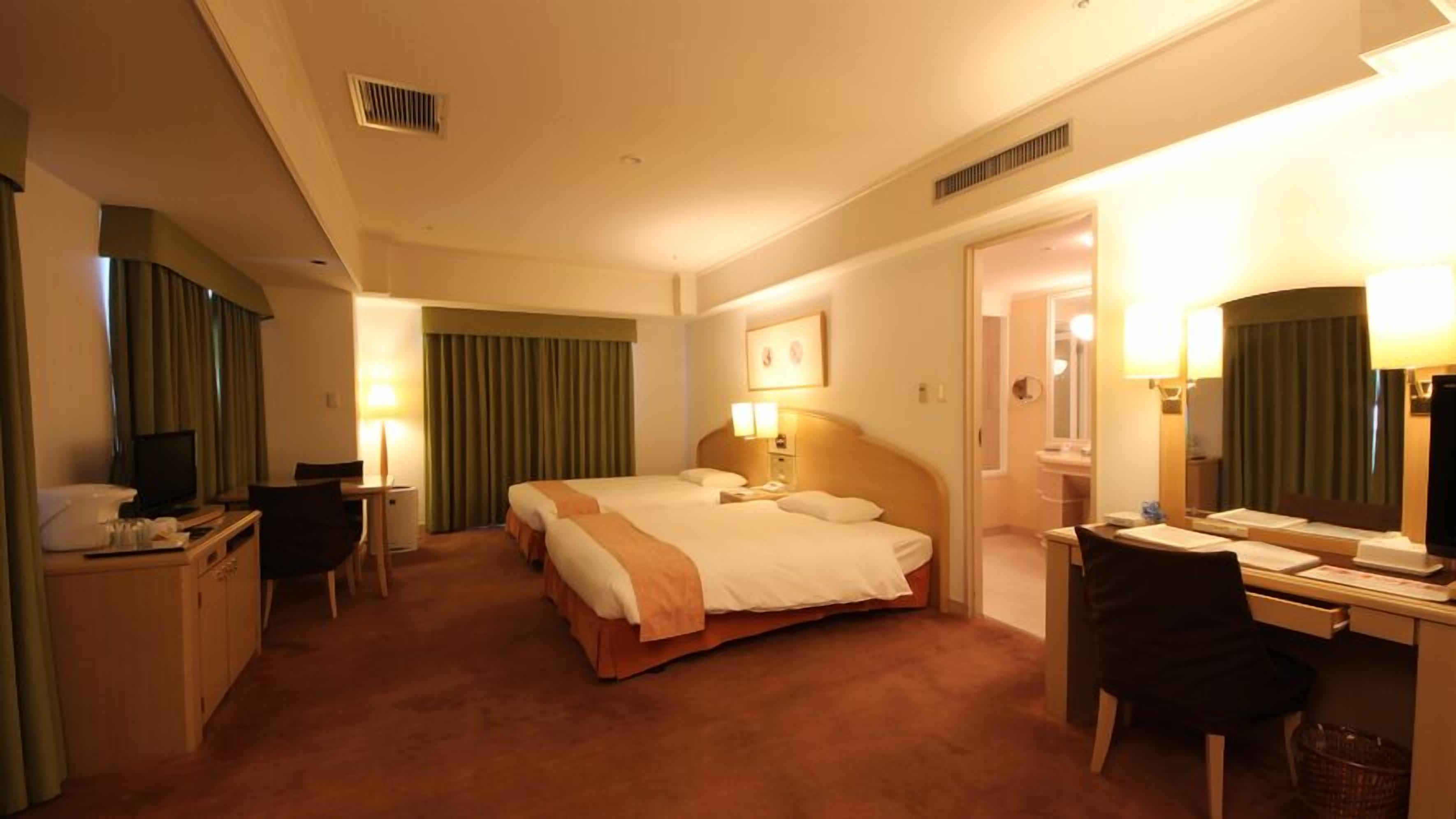 A hotel room with a bed, desk, chair, television, and a bathroom visible through an open door.