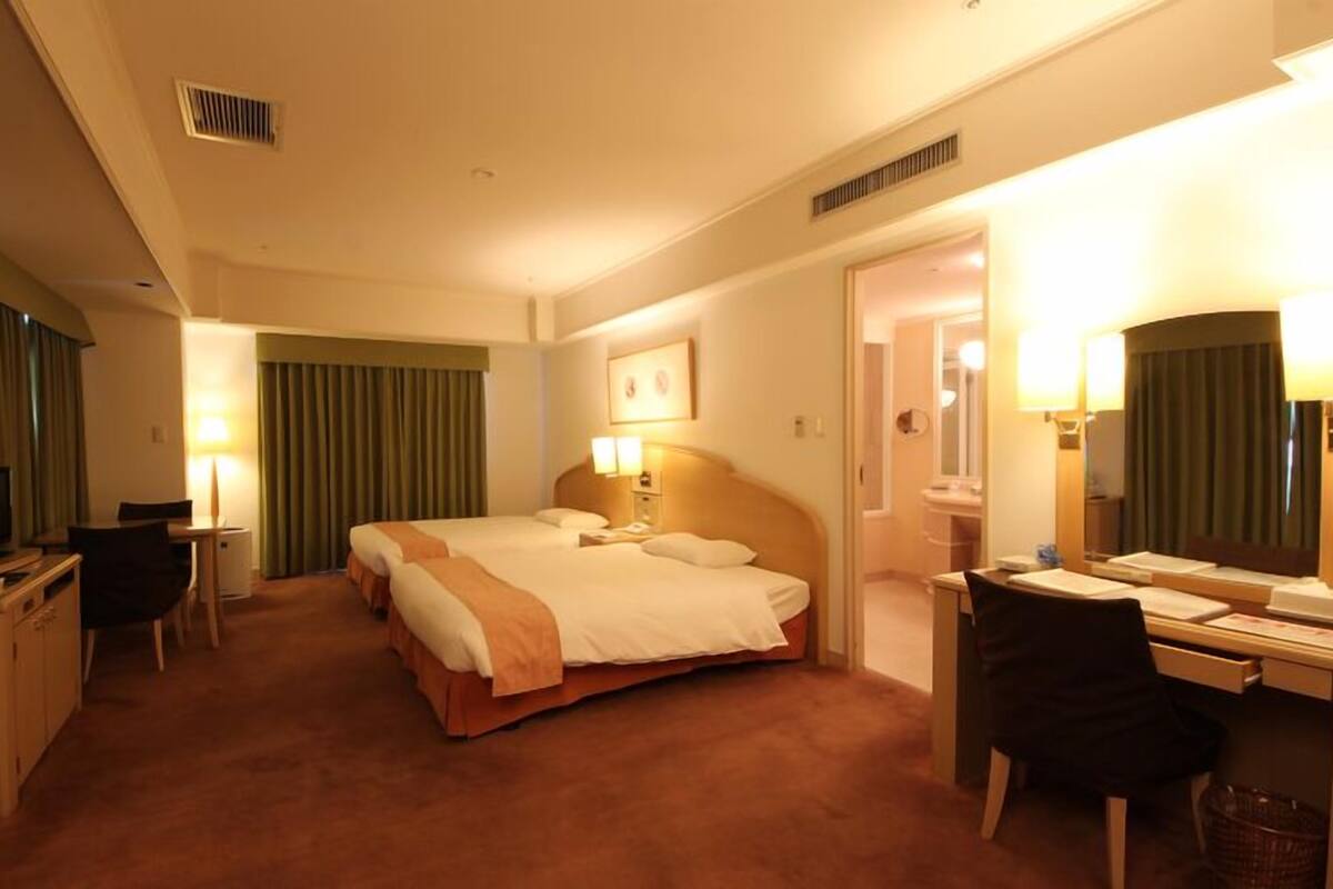 Habitación de hotel con cama, escritorio, silla, televisor y baño visible a través de una puerta abierta.
