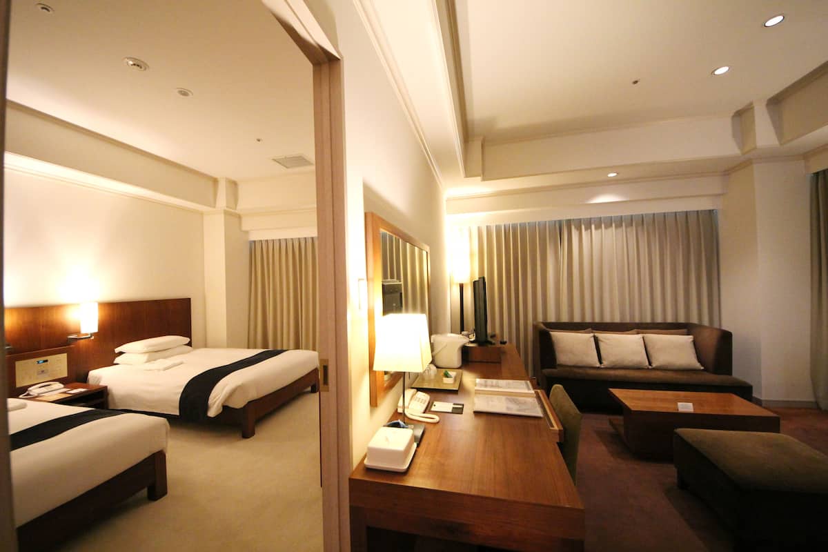 Habitación de hotel con dos camas, un sofá, un escritorio con teléfono y una lámpara.