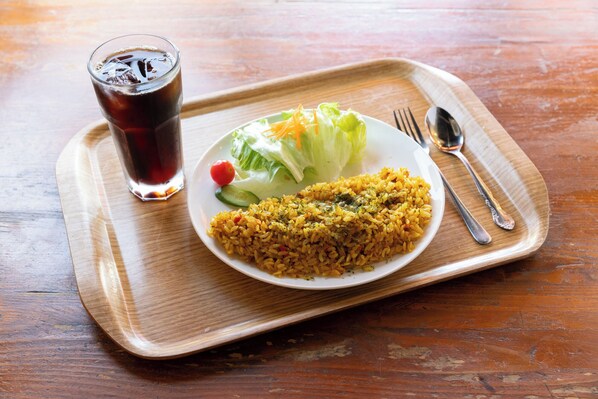 Une assiette de riz jaune accompagné de légumes et un verre de thé glacé, le tout posé sur un plateau en bois.