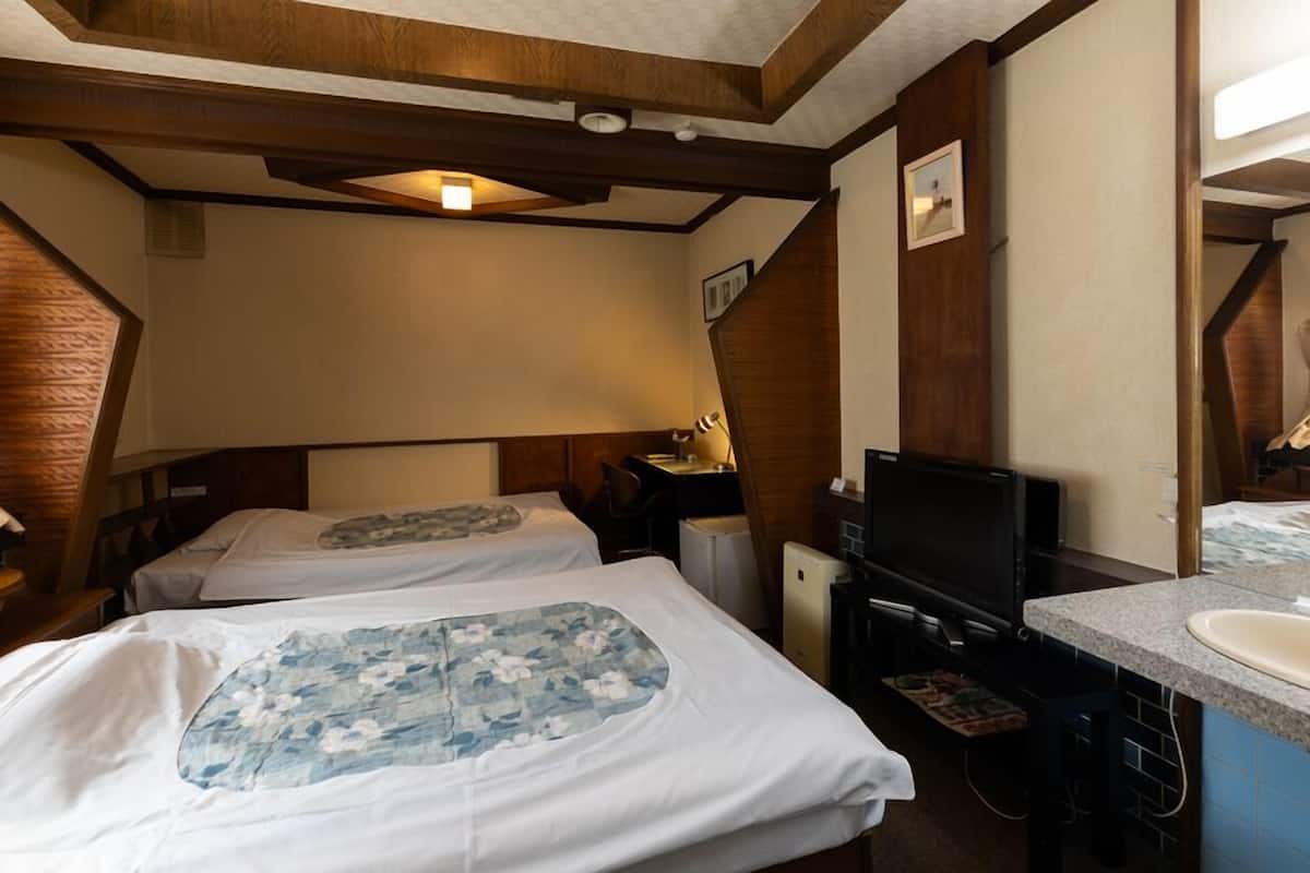 Habitación de hotel con dos camas, televisor, escritorio y baño con lavamanos.