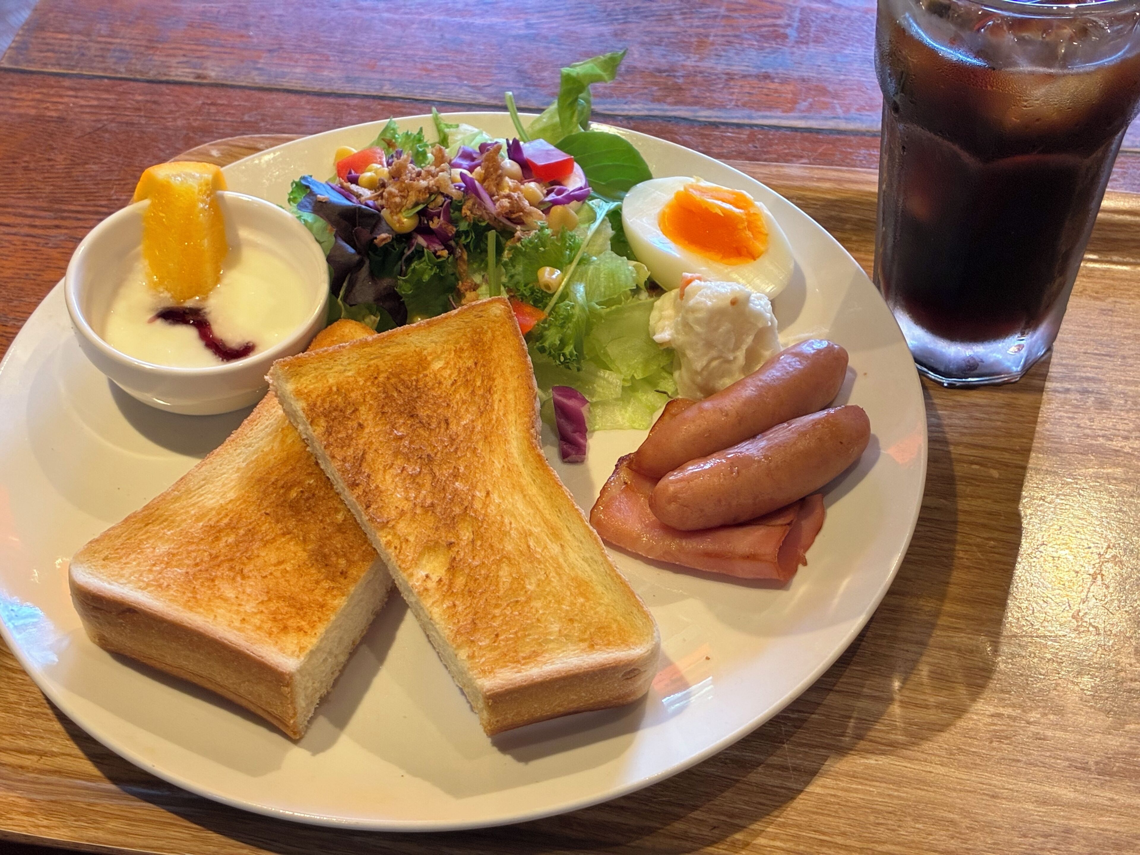 A plate with toast, a salad, a boiled egg, and sausages.