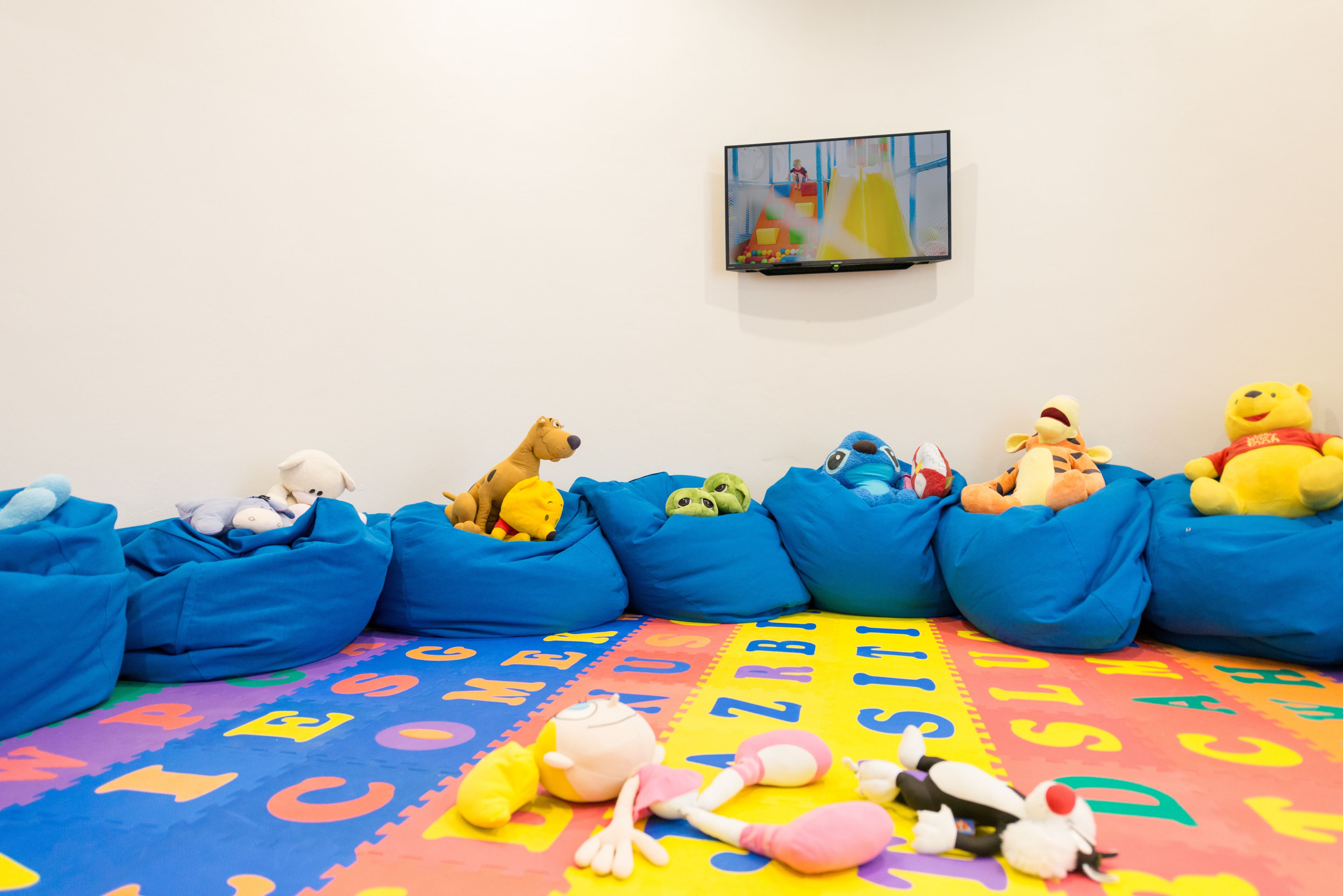 A children's play area with colorful foam mats, bean bags, and plush toys.