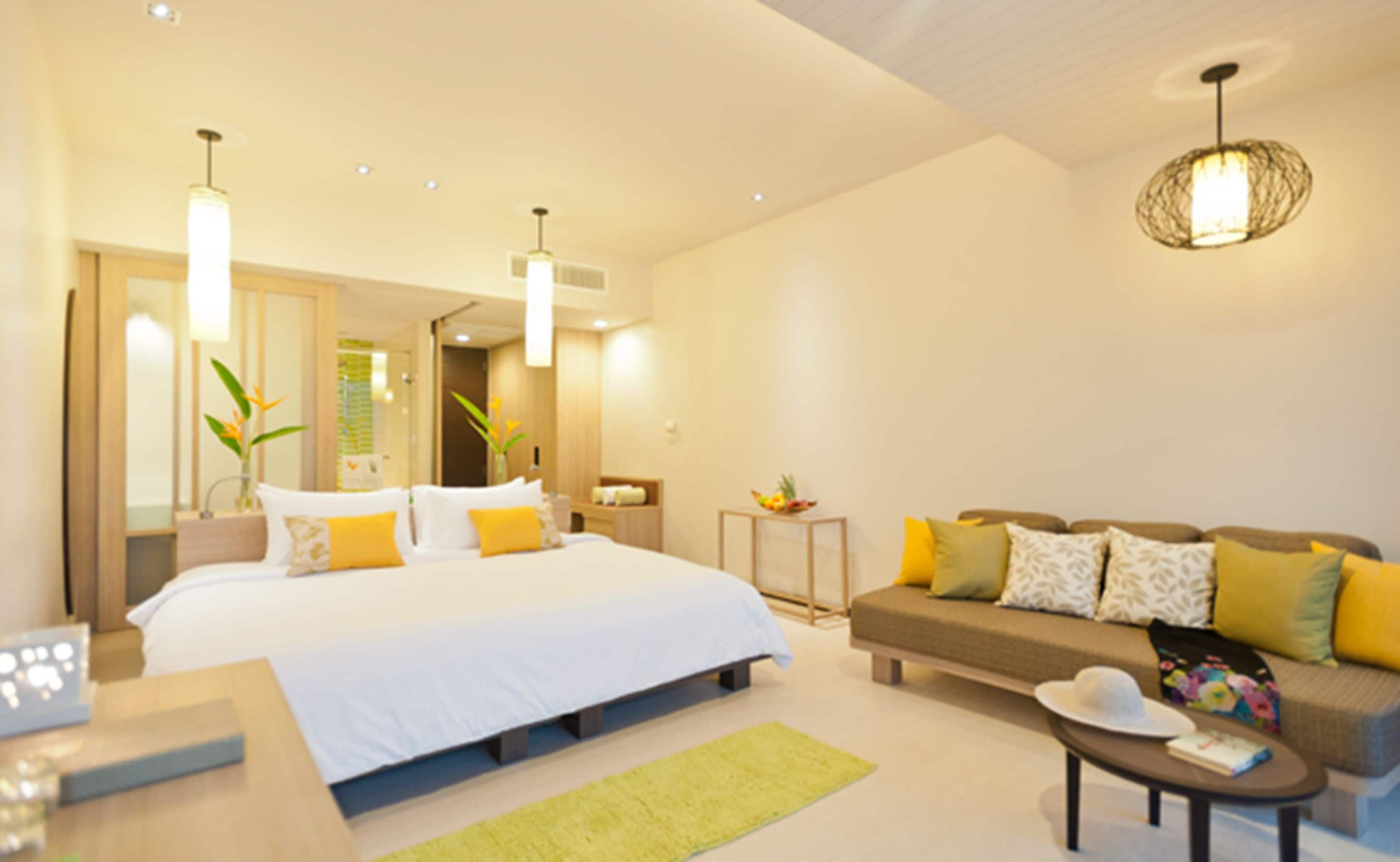 A modern hotel room with a large bed, a sofa, a coffee table, and a dining table.