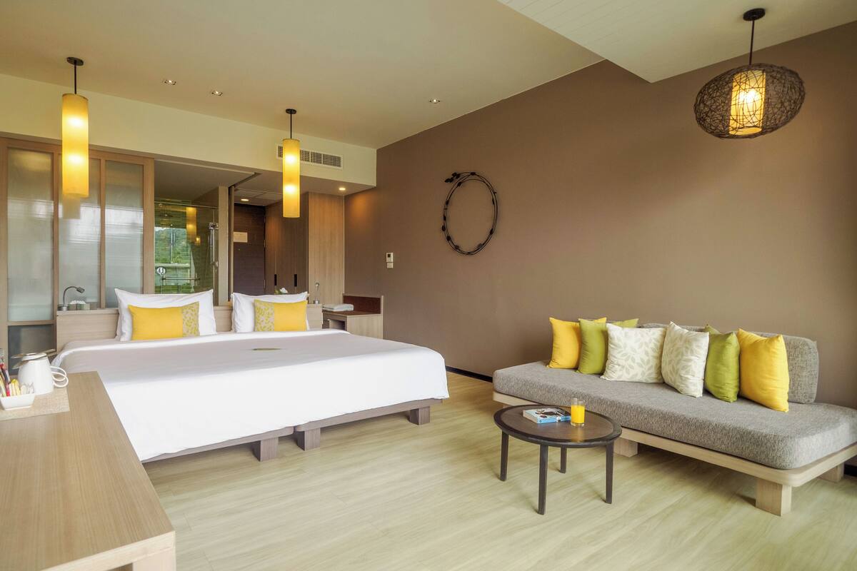 A modern hotel room with a large bed, a sofa, a coffee table, and a shower area.