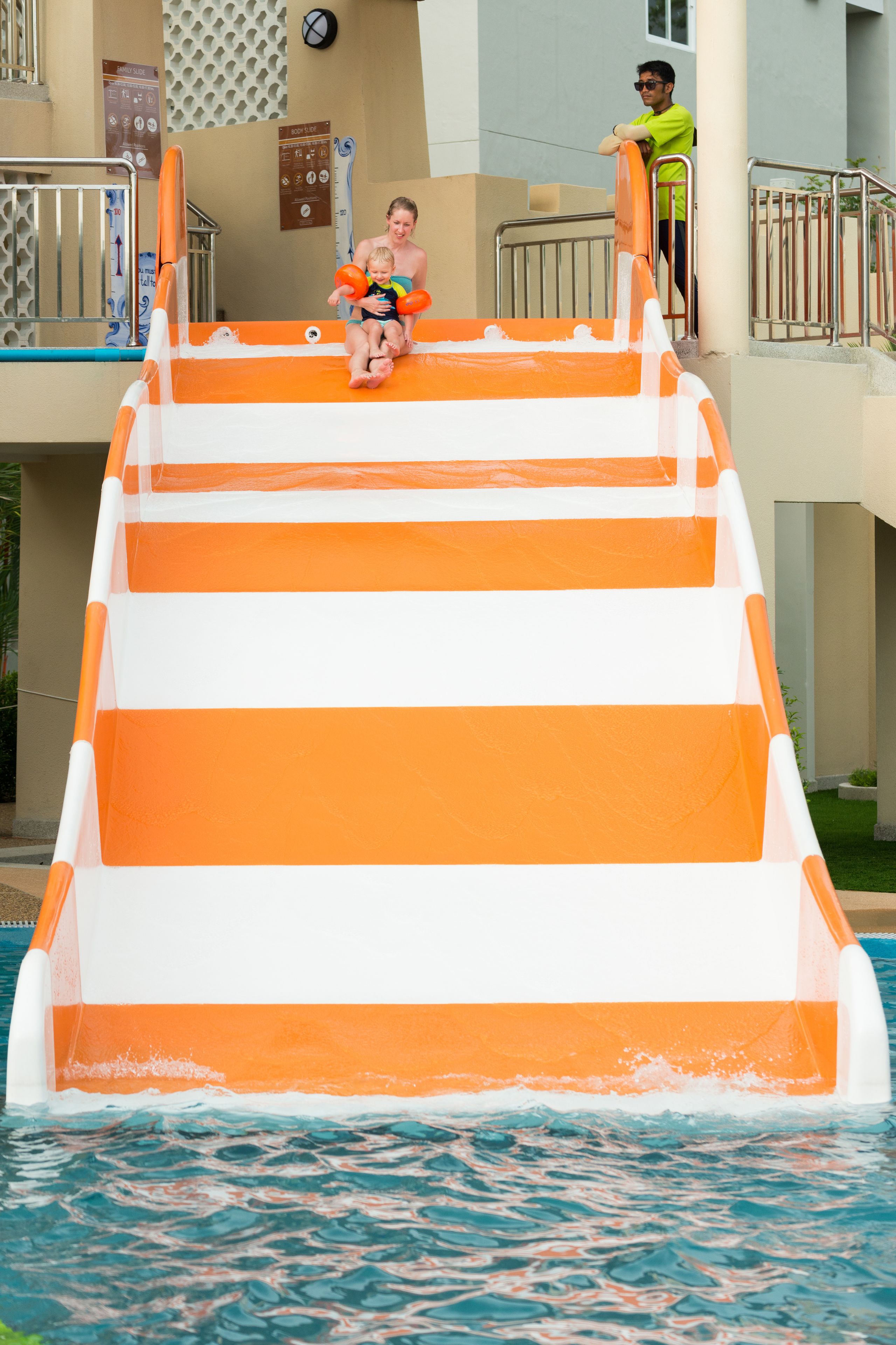 A water slide with orange and white stripes, a pool, and a building with a sign in the background.
