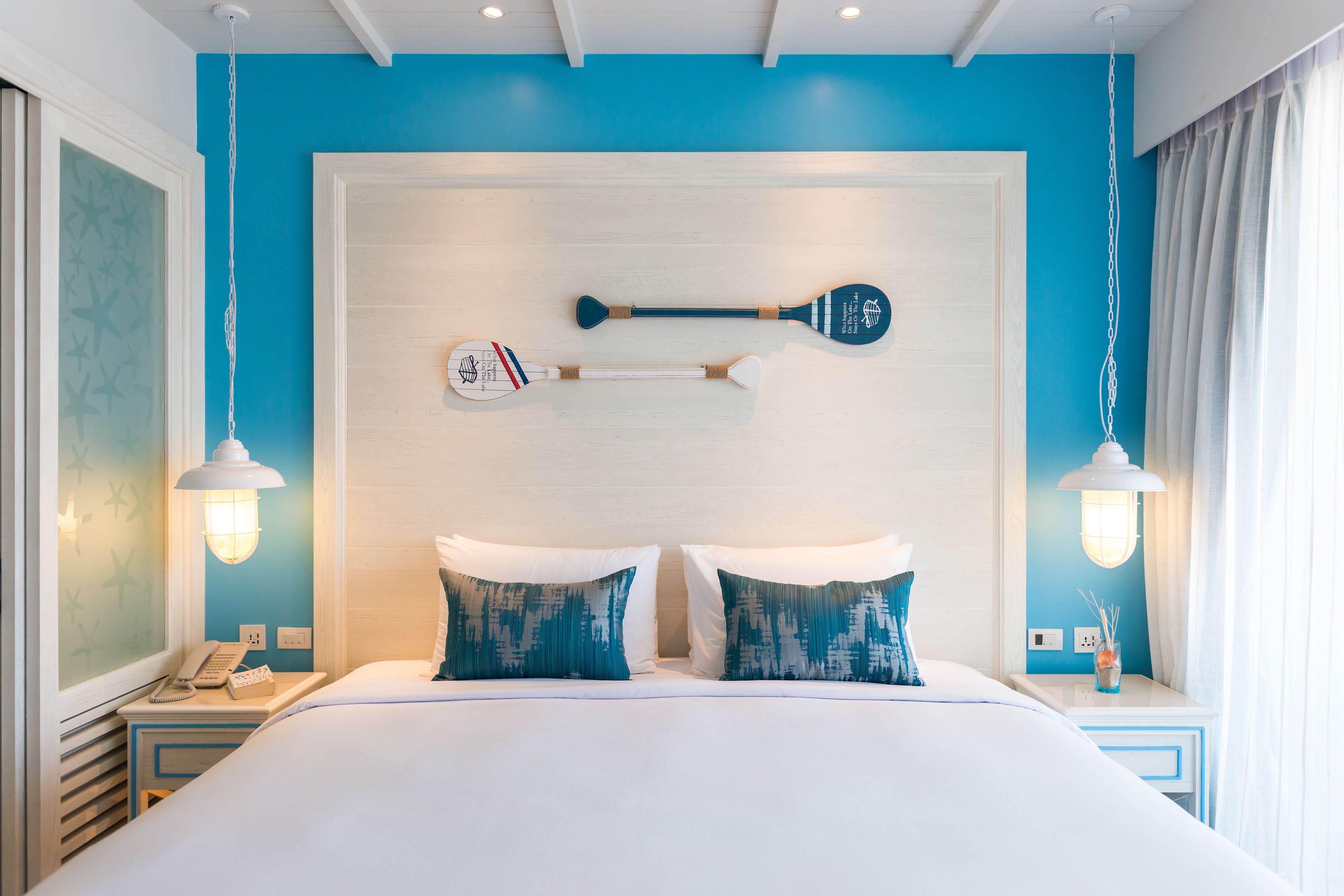 Una habitación de hotel moderna con una cama grande, dos mesitas de noche, un estante en la pared con palas y una ventana con cortinas.