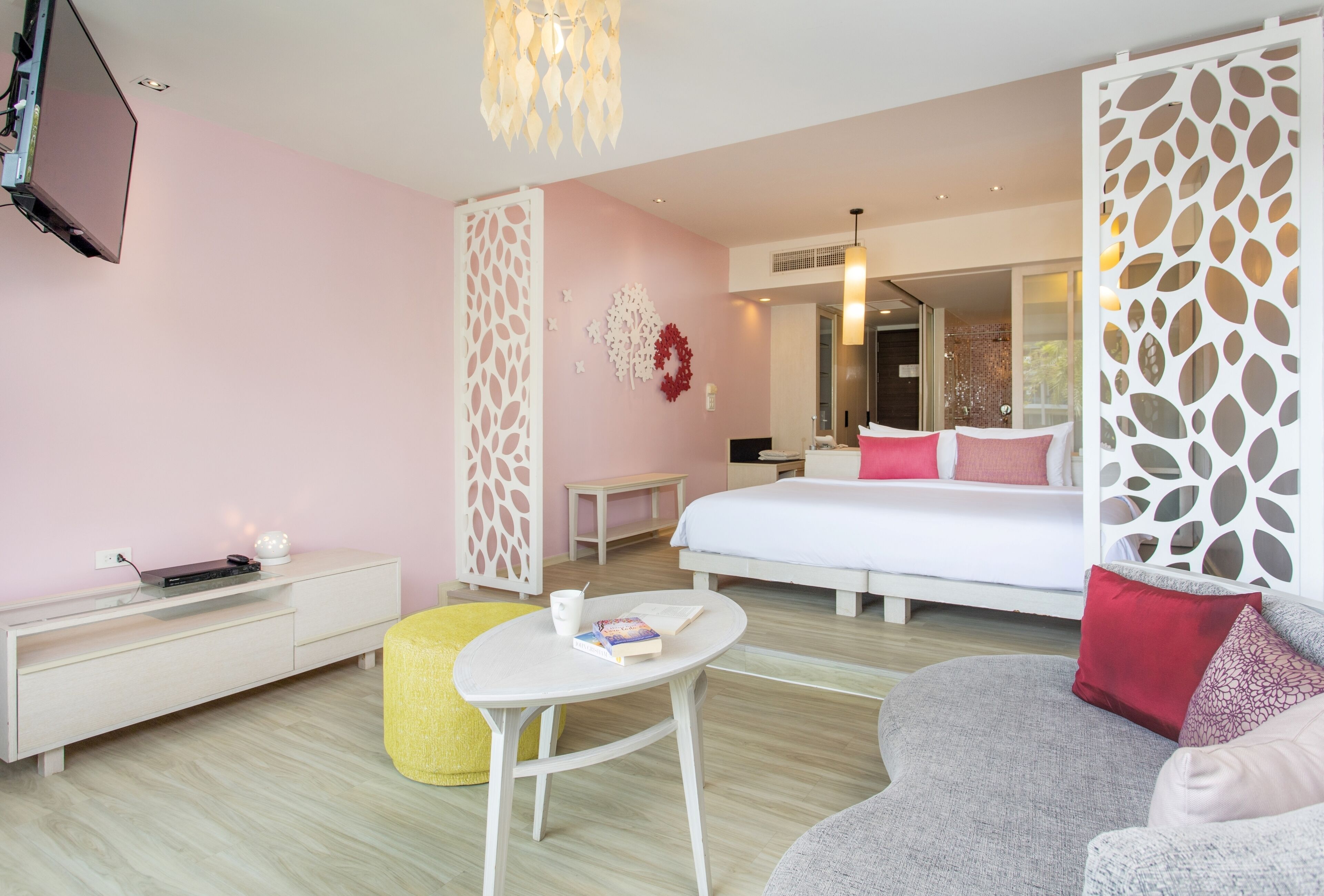 Quarto de hotel moderno com uma cama, um sofá, uma mesinha e uma televisão fixada na parede.