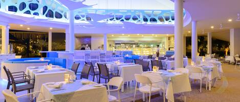 Un amplio comedor interior con varias mesas y sillas, una zona de bar central y un diseño de techo distintivo.