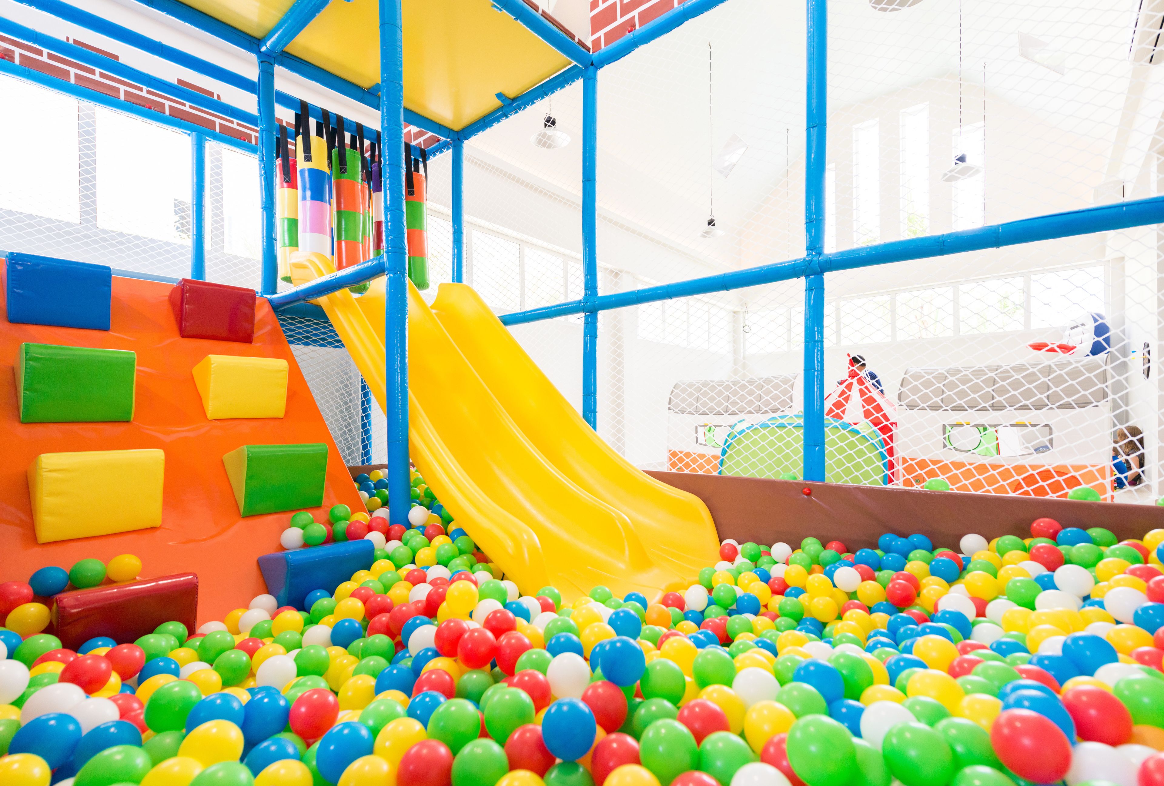 Un área de juegos con un tobogán amarillo, bloques de espuma de colores y una piscina de pelotas llena de bolas multicolores.