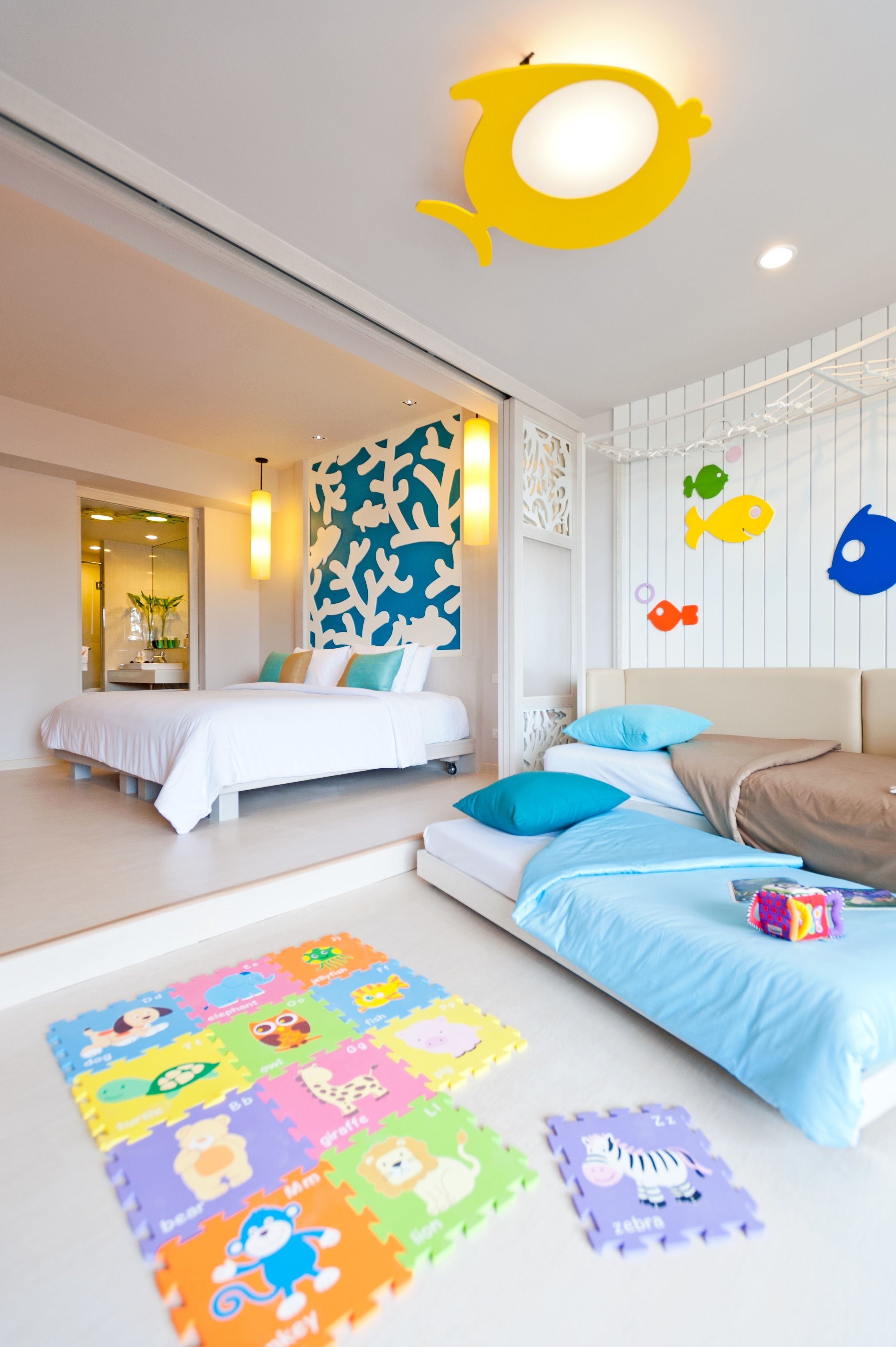 A modern bedroom with a large bed, a smaller bed, and a colorful play mat.