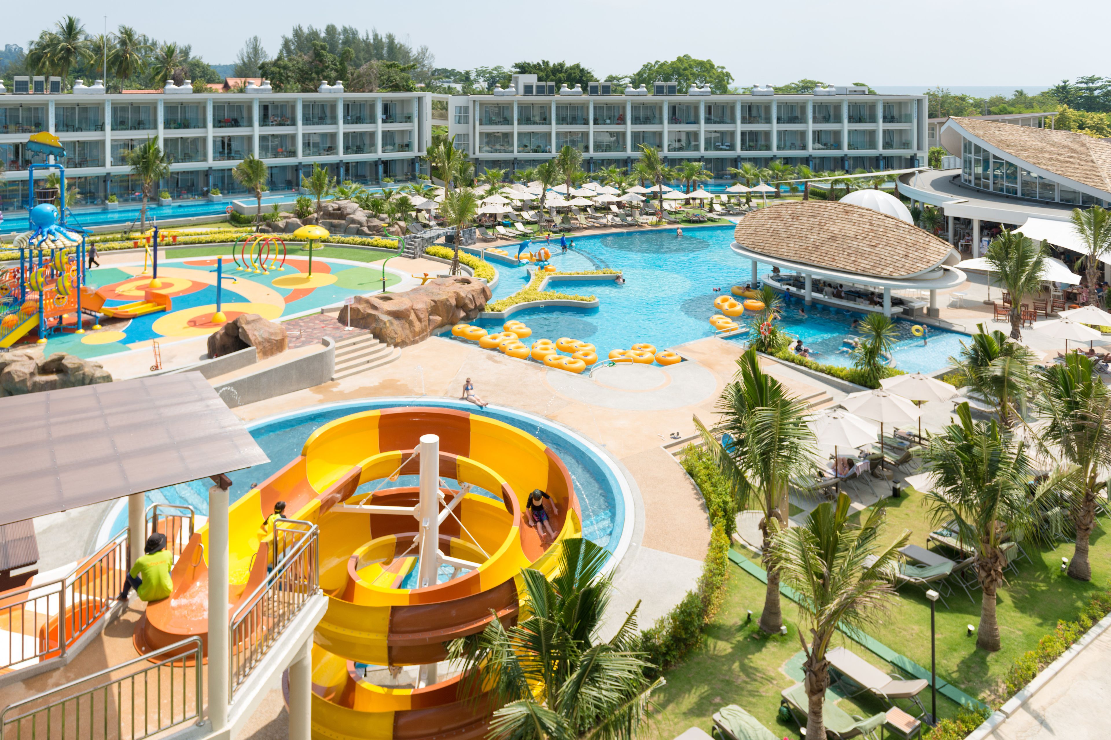 Ein Poolbereich eines Resorts mit Rutschen, einem Wasserpark und einem Mehrstöckgebäude mit Balkonen.