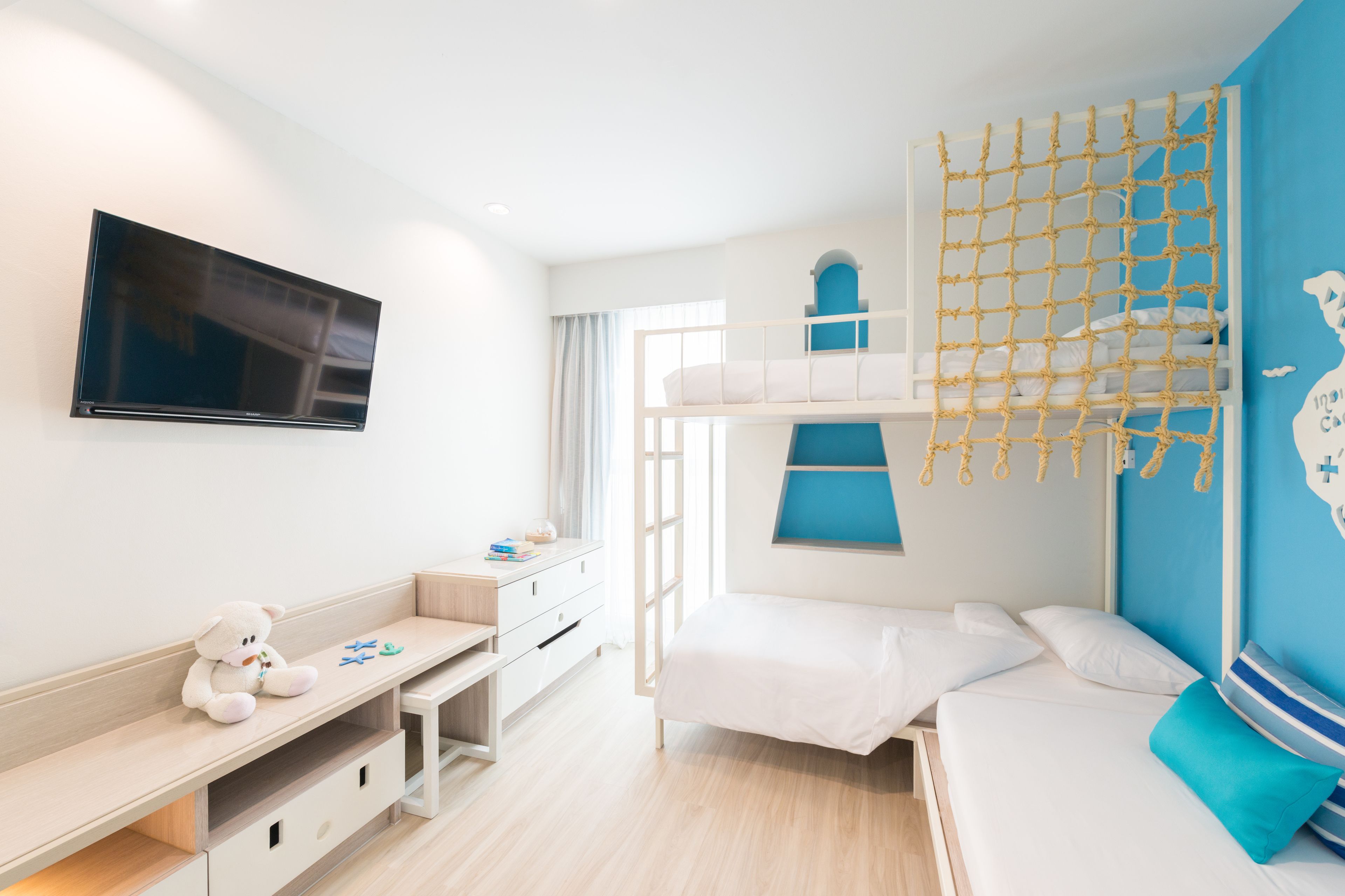 Un dormitorio infantil con literas, un televisor, un escritorio y una ventana.
