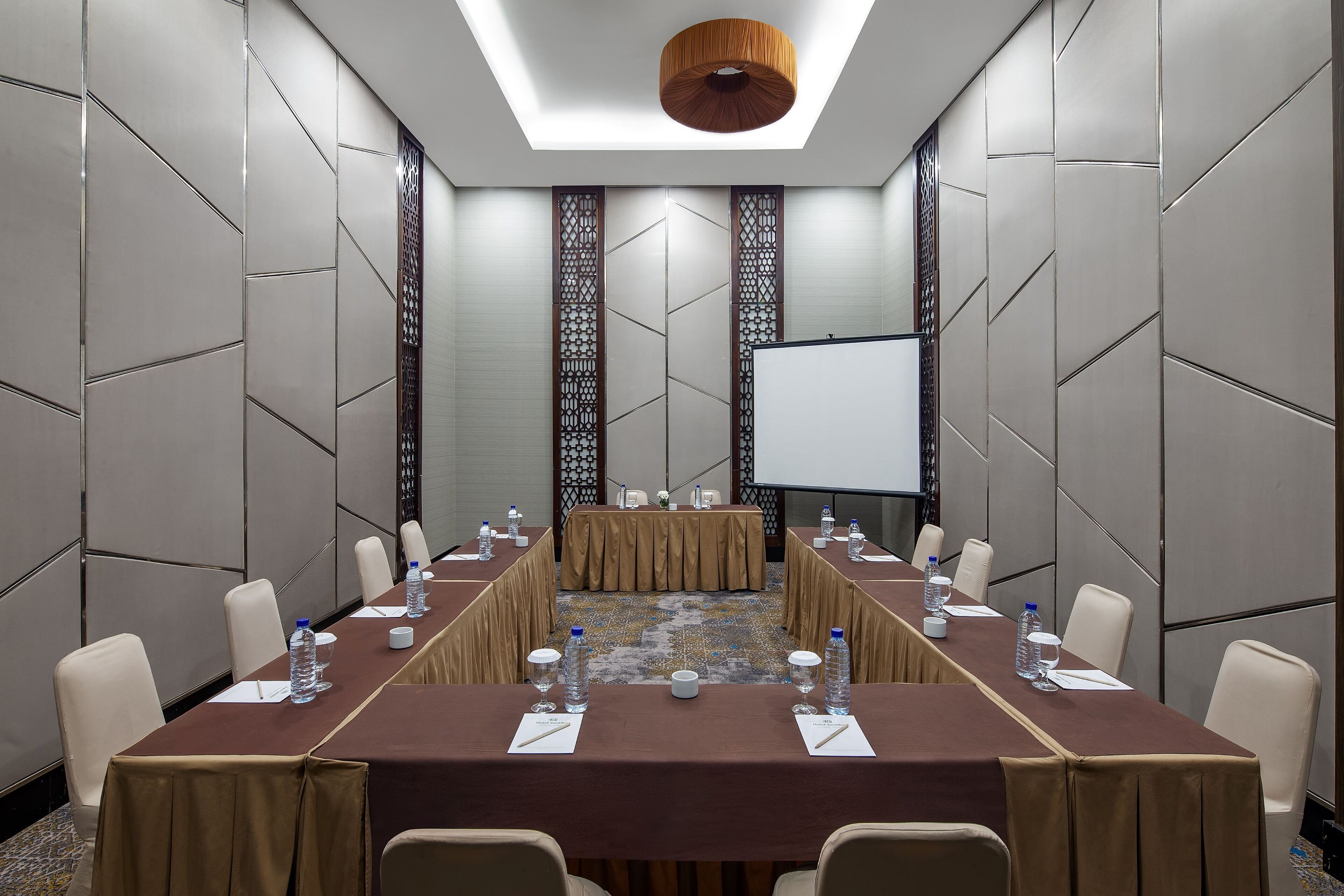 A conference room with a long table, chairs, water bottles, and a projector screen.
