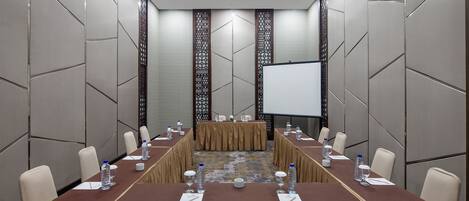 A conference room with a long table, chairs, water bottles, and a projector screen.