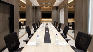 A conference room with a long table, black chairs, water bottles, and a large screen.