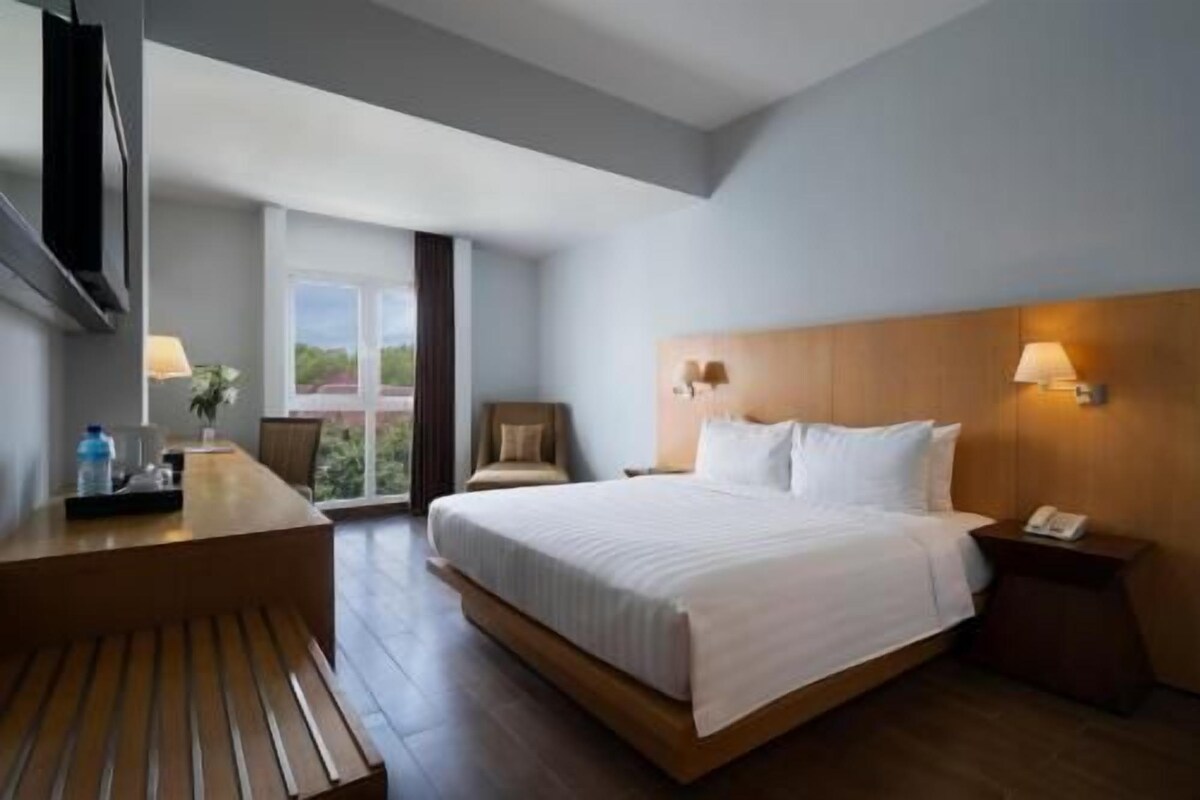 Ein Hotelzimmer mit einem großen Bett, einem Schreibtisch, einem Stuhl und einem Fenster mit Blick.