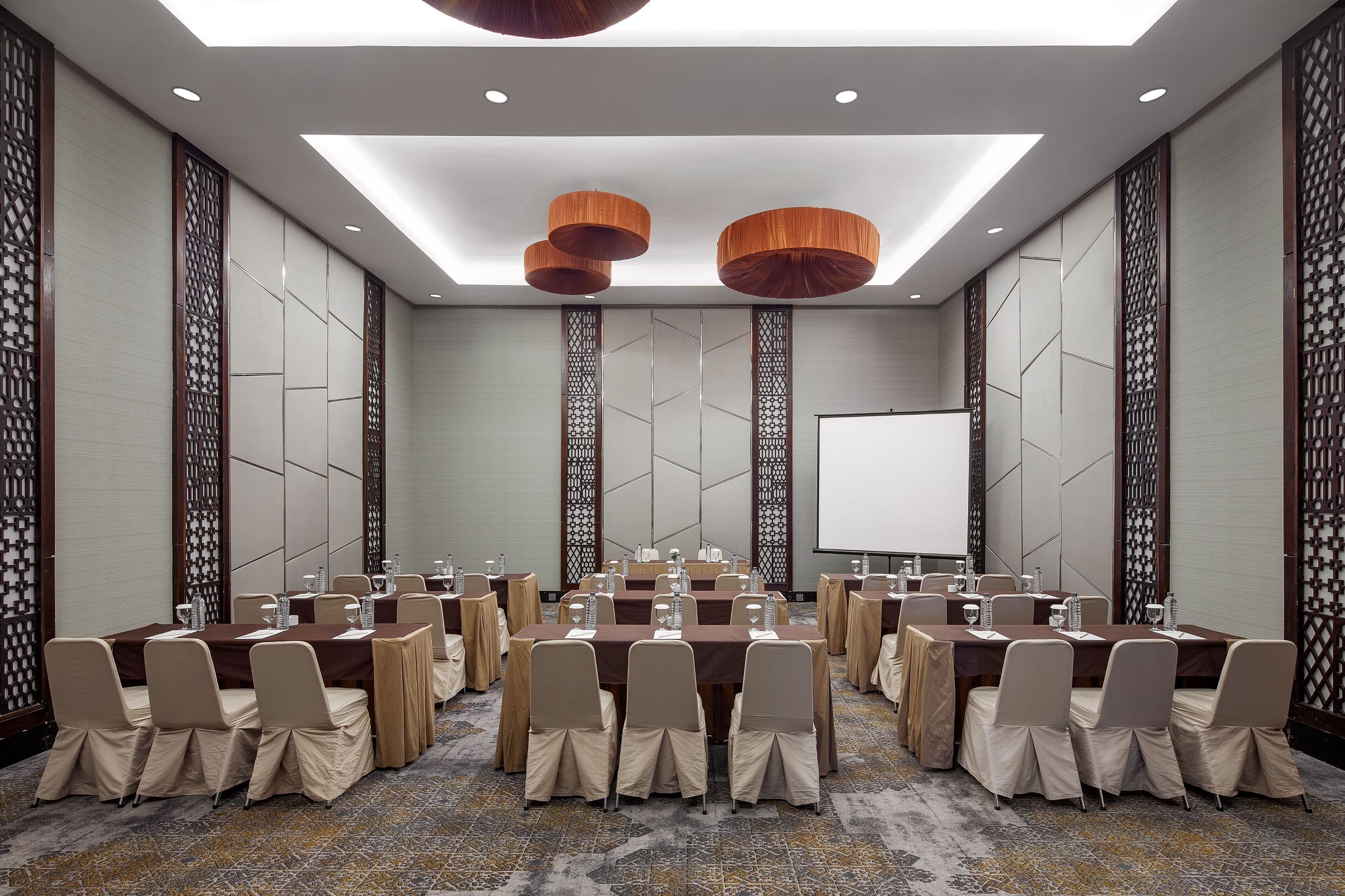 A conference room with multiple tables and chairs, equipped with water bottles and nameplates, and a large screen at the front.