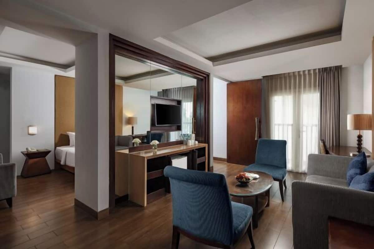 A hotel room with a wooden floor, a dining area with a table and chairs, a TV, and a large mirror.