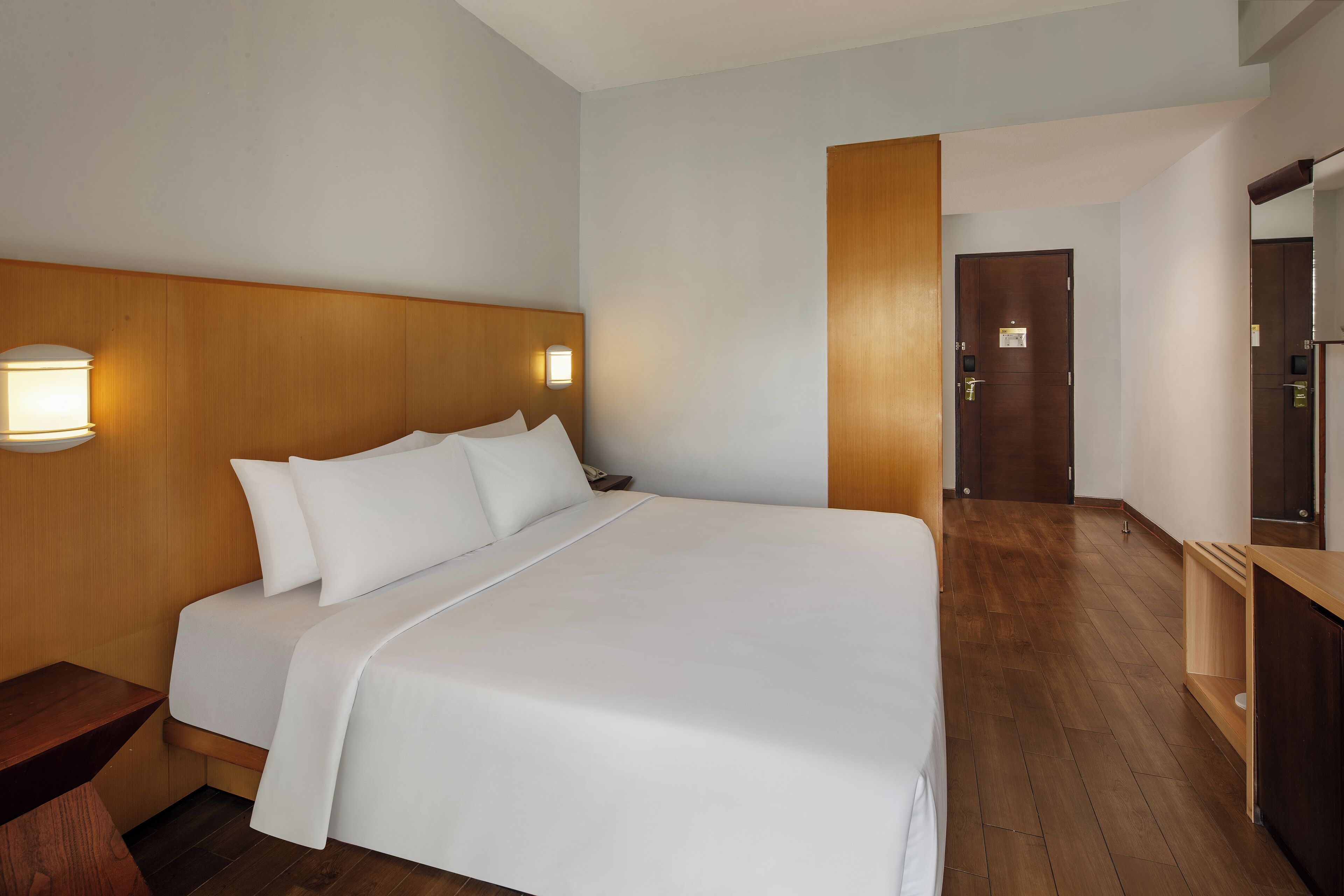 A hotel room with a large bed, wooden headboard, bedside table, and a nightstand.