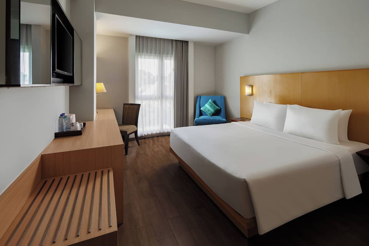 A hotel room with a large bed, a desk, a chair, a TV, and a window with curtains.