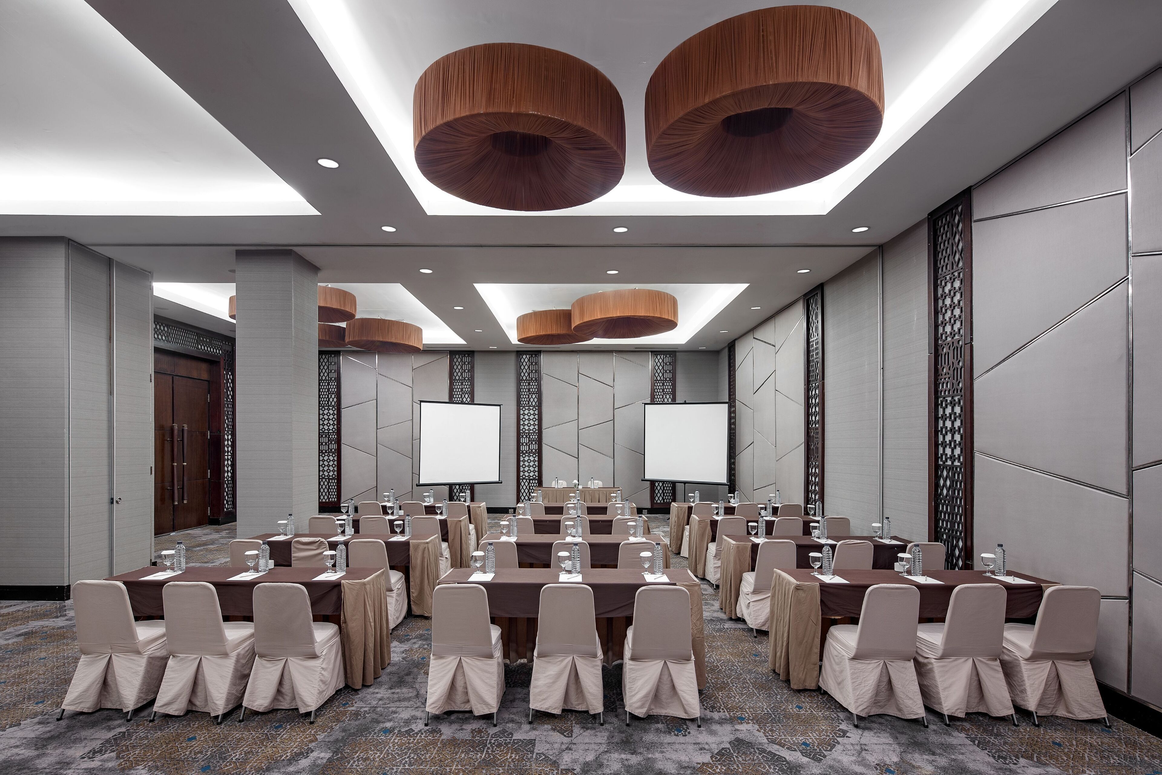 A conference room with multiple tables, chairs, and a large screen.