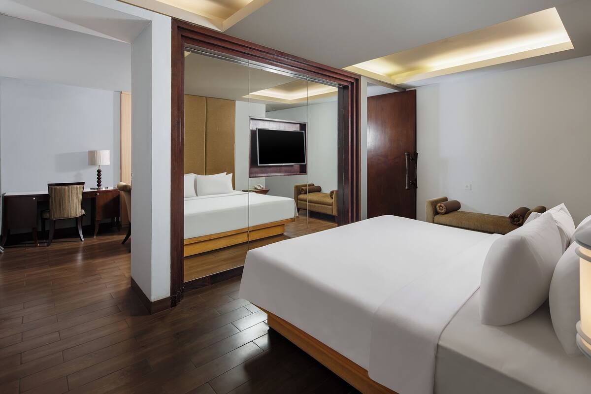 A hotel room with a large bed, a TV mounted on the wall, a desk with a chair, and a wooden floor.