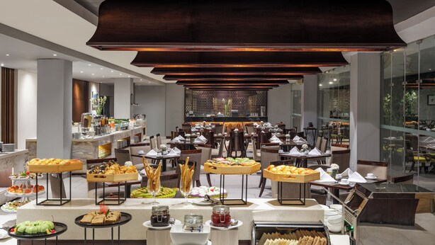 A modern hotel dining area with a buffet setup, including various food stations and seating arrangements.