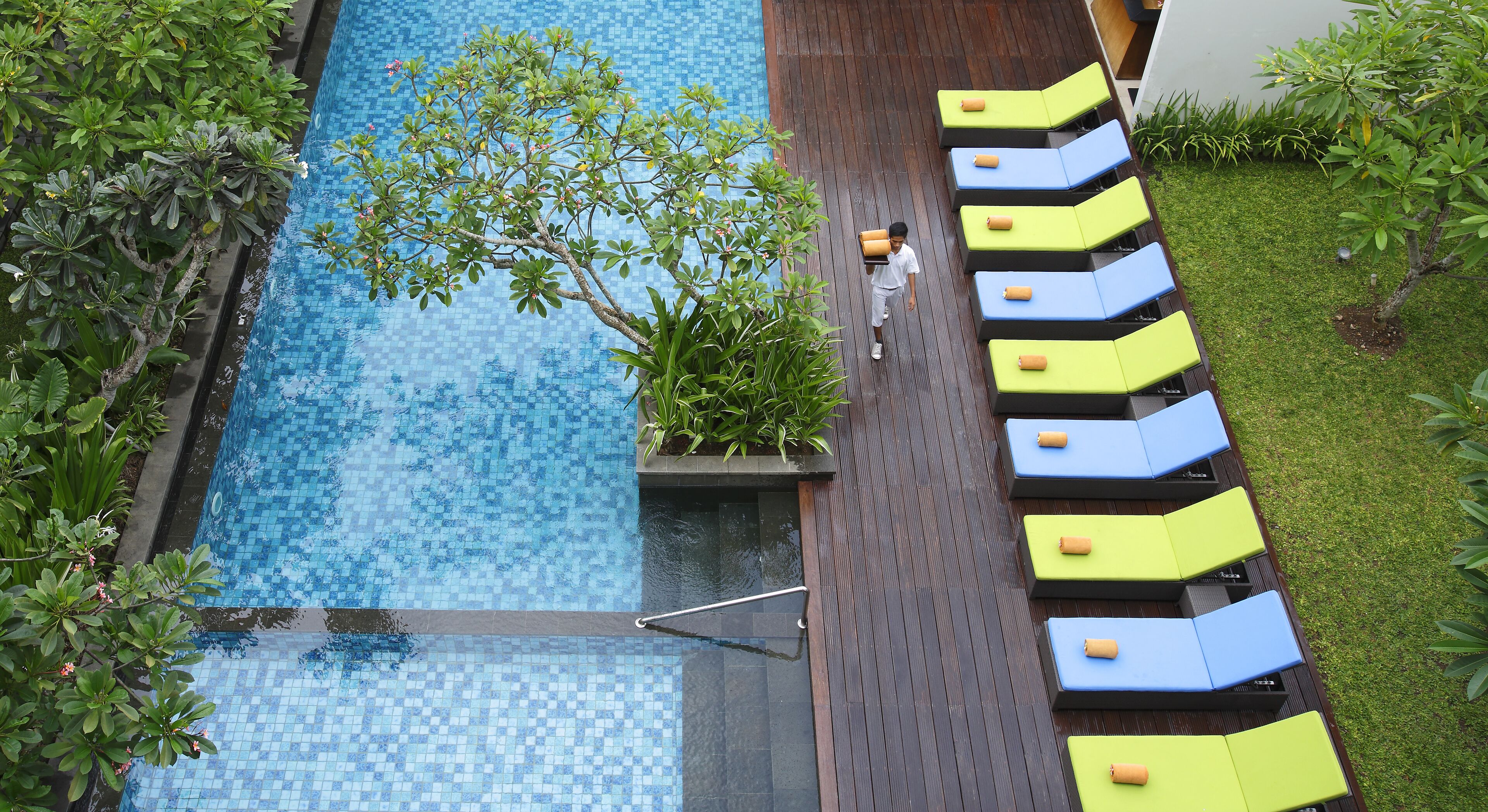 A swimming pool with a tiled deck, surrounded by greenery and lounge chairs.