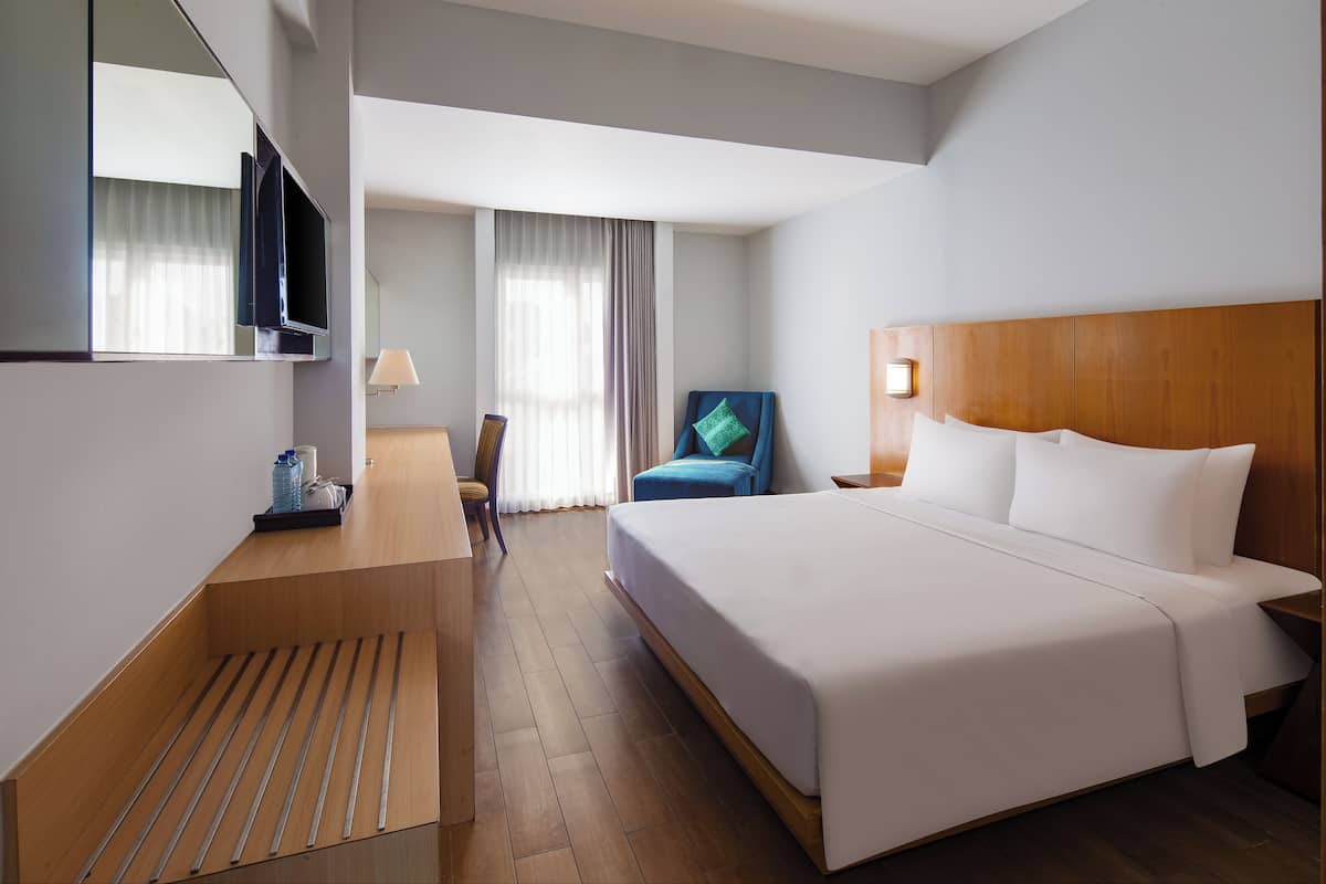 A hotel room with a bed, a desk, a chair, a TV, and a window with curtains.